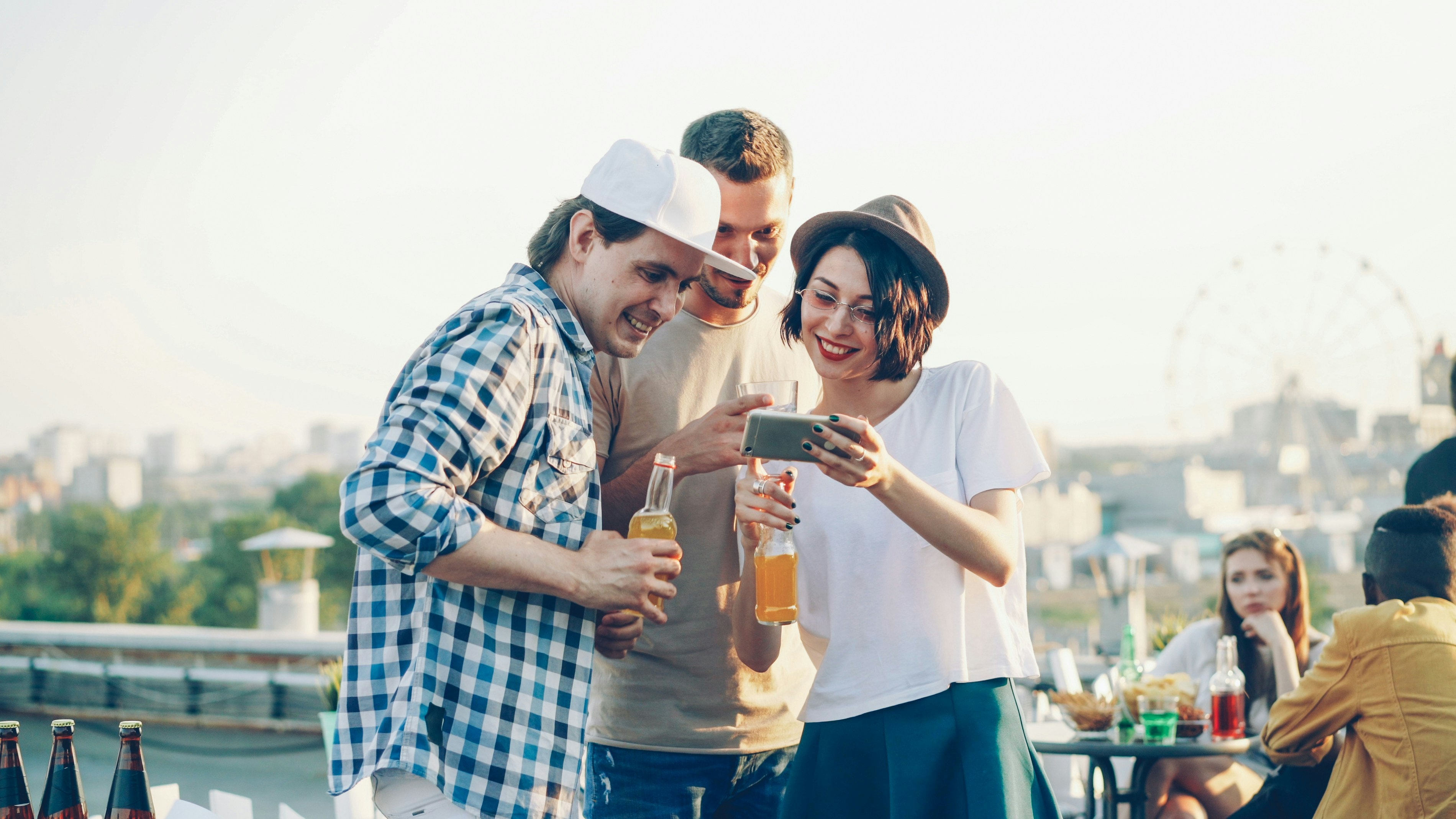 Groupe d'amis riant en soirée sur un rooftop, en train de configurer un blind test Bliā sur téléphone